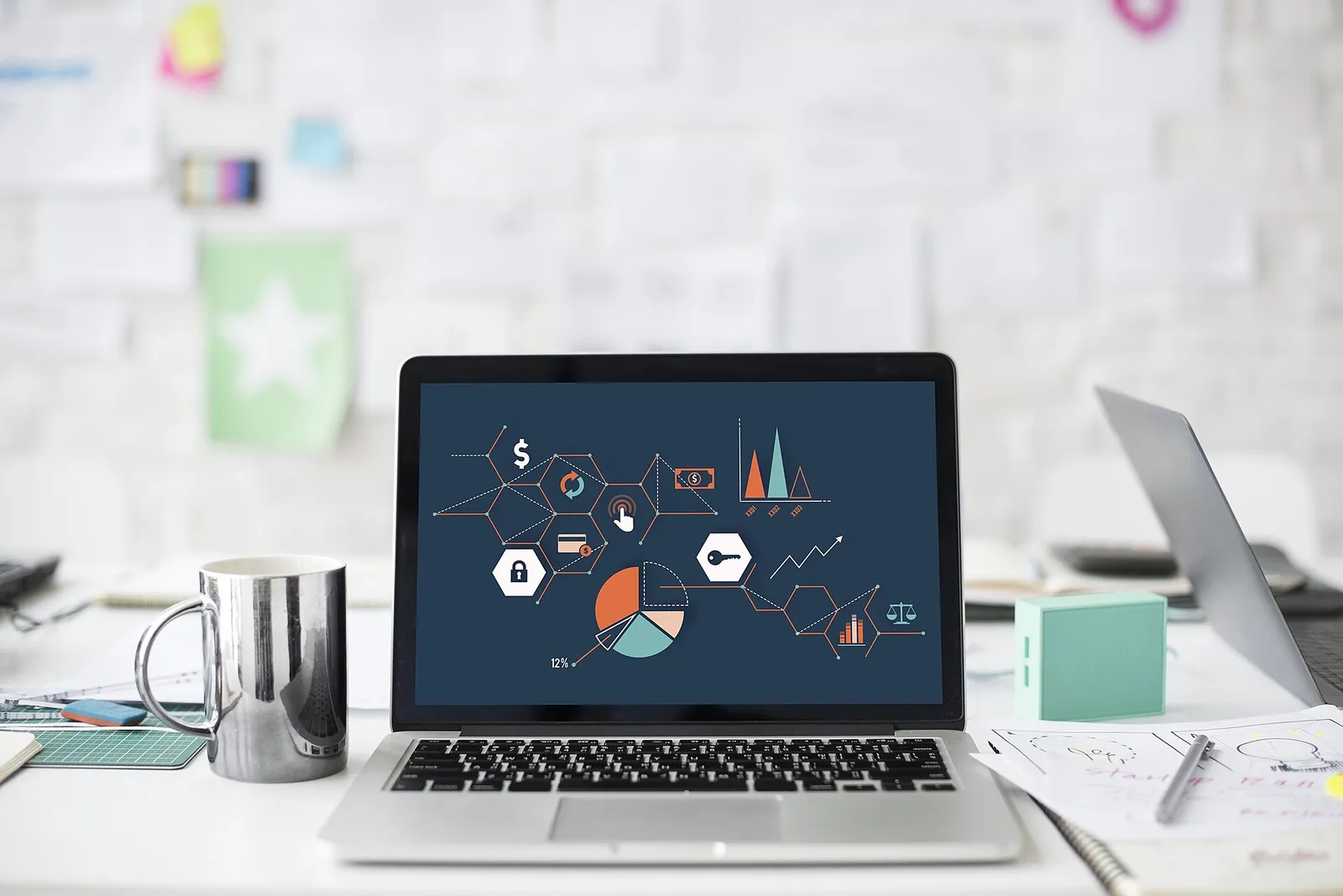 Laptop di meja yang penuh berkas menampilkan beberapa grafik